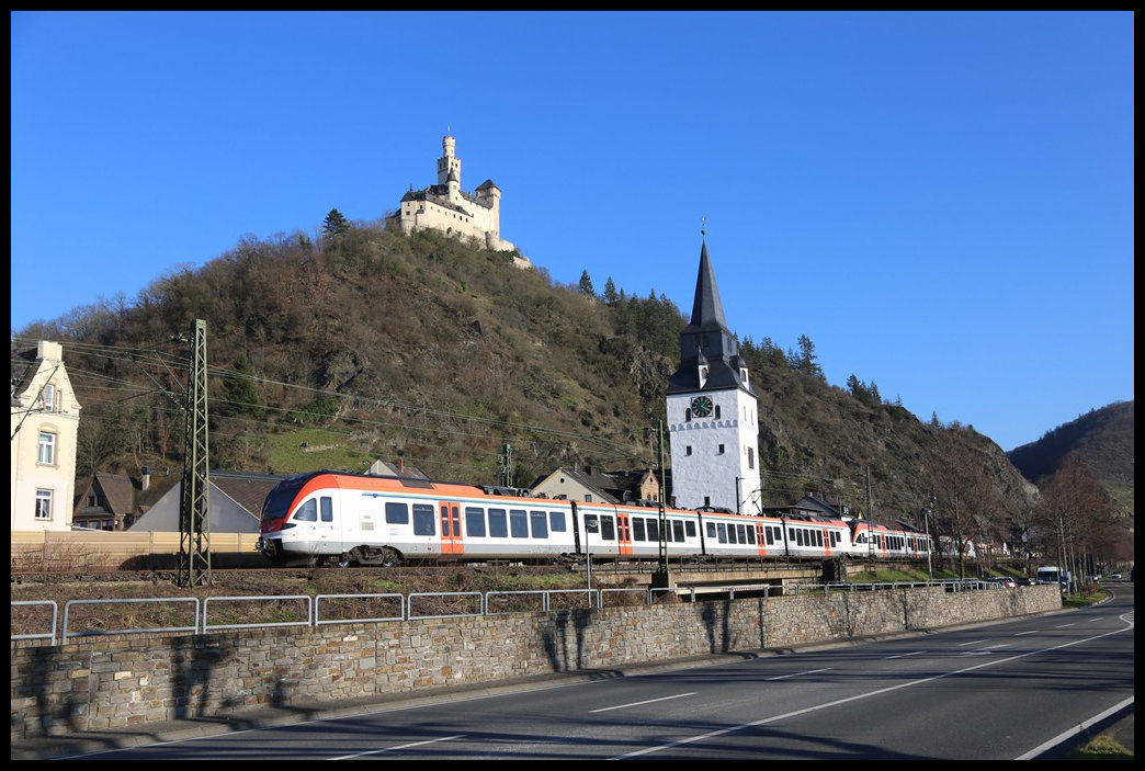 Von oben grüßt hier am 1.3.2023 die Marksburg während darunter ein zweiteiliger Zug von VIAS um 16.06 Uhr den Bahnhof Braubach bzw. den Ort rechtsrheinisch in Richtung Frankfurt am Main verlässt. 