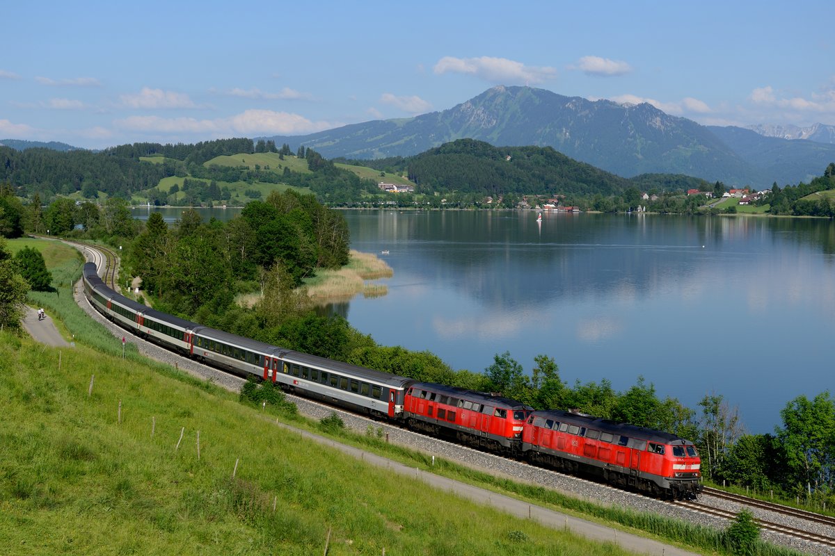 Von der Realisierung dieses Fotos habe ich schon lange geträumt. Am 16. Juni 2013 kamen dann ein paar günstige Faktoren zusammen: EC 192 nimmt baustellenbedingt nicht den üblichen Weg über den  Ho-Chi-Minh Pfad , sondern fährt über Kempten. Weil Sonntag ist, hat der Zug acht Wagen und es sind auch zwei 218-er vorgespannt. Das Wetter passt, die Wolken drapieren sich bildgestaltend über dem Grünten und nicht vor der Sonne und die kleine Strasse bleibt auch frei. Klick, richtig ausgelöst, Fotograf zufrieden!