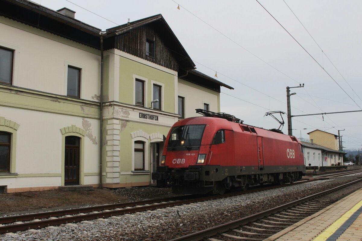 Vor dem alten Aufnahmegebäude des Bahnhofs Ernsthofen steht am 27.2.2024 die 1116 127, die als Lokzug von Graz nach Linz zur dortigen HW fuhr und wartet auf eine Zugkreuzung und die Weiterfahrt.
