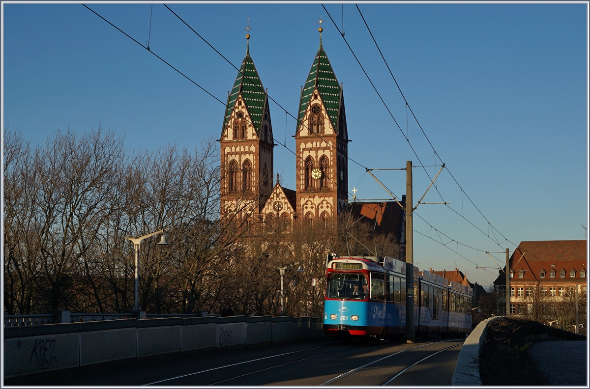 Vor dem Hintergrund der Kath. Kirche  Herz-Jesus  in Freiburg im Breisgau erreicht ein VAG  Strassenbahn-Zug in Kürze die Haltestelle Hauptbahnhof. 

29. Nov. 2016
