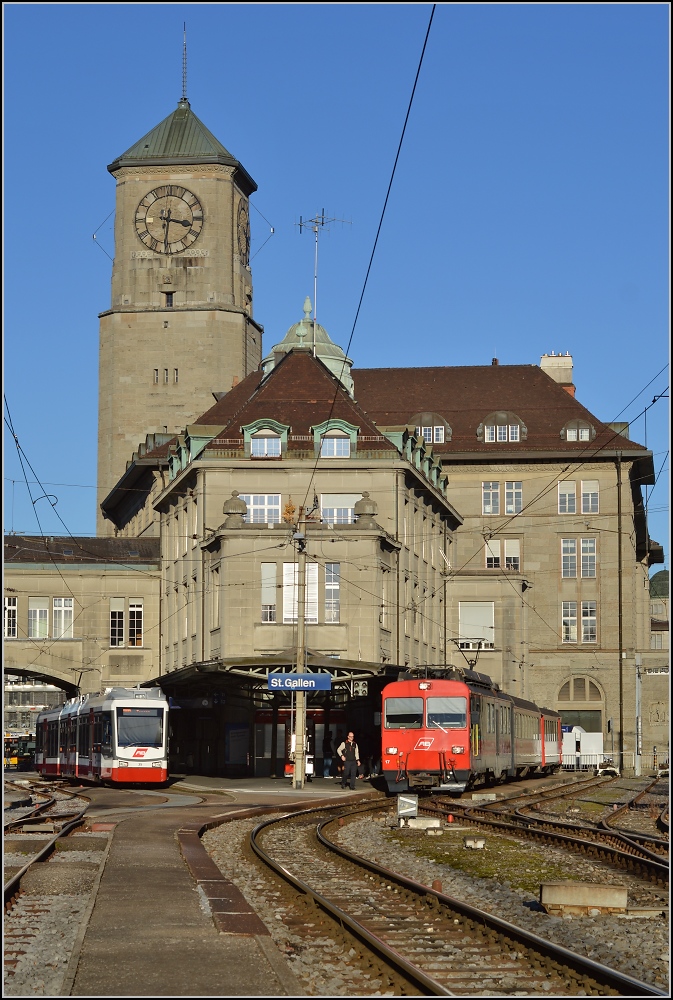 Vor dem imposanten Appenzellerbahnhof in St.Gallen. Links die Trogenerbahn, rechts die Appenzellerbahn. In zwei Jahren wird des hier völlig anders aussehen, denn die Durchmesserlinie wird die beiden getrennten Bahnen verbinden. So entsteht links ein zweiter Bahnsteig, damit sich hier die Züge kreuzen können. Die Gleise rechts werden für Parkplätze verschwinden. Heute haben die beiden Bahnen ausser der Spurweite nicht viel gemeinsam. Die Züge der Appenzellerbahn können nicht auf den Straßenbahngleisen der Trogenerbahn verkehren, bei der Appenzellerbahn müssen dann Weichen angepasst werden und der Zahnstangenabschnitt verschwindet in einem zahnstangenfreien Tunnel. Die Fahrdrahtspannung muss auch angeglichen werden. November 2014. Für Zweifler, das Bild ist vom öffentlich zugänglichen Bahnsteig entstanden.