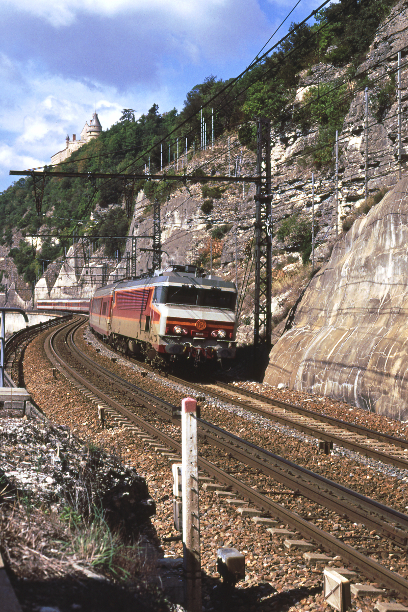 Vor dem TGV-Zeitalter war der Rapide  Le Capitole  Paris - Limoges - Toulouse der Paradezug der SNCF. Er fuhr als erster mit 200 km/h - im Abschnitt Les Aubrais - Verzon - und war mit Grand Confort-Waggons ausgestattet. Geführt wurde er natürlich von Loks der Reihe CC6500. Hier ist die CC6505 mit dem  Le Capitol du Matin  nach Toulouse im Tal des Lot unterwegs. Ein Teil der Waggons ist zu Wagen der zweiten Klasse umgebaut. Über dem Zug erkennt man das Schloß von Mercues.
Cahors (Lot), Oktober 1989; Canon A1, digitalisiert mit Canoscan
