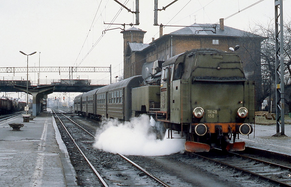 Vor einem Personenzug nach Olesnica steht Tkt48 158 im Februar 1989 abfahrbereit im etwas trist wirkenden Bahnhof Kepno. Auch die olivgrüne Lackierung der Lok bringt keinen wirklichen Farbtupfer ins Bild.