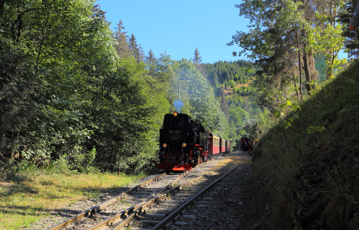 Vorbeifahrt von 99 7235 mit P8964 (Eisfelder Talmühle - Quedlinburg) am 07.07.2018 am Unterberger Steinbruch. (Bild 2) Wie stark sich die anhaltende Trockenheit des Sommers 2018 auch im Harz ausgewirkt hat, sieht man am aufgewirbelten Staub unterhalb des Zuges. Selbst beim Laufen staubte es unter den Füßen, was ich in dieser Form im eigentlich eher feuchten Harz, noch nie erlebt habe.