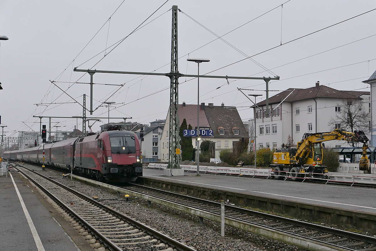 Whrend 1116 156 mit den Wagen des RJX 897  BREGENZERWALD  von Frankfurt (Main) zum Flughafen Wien in den Friedrichshafener Stadtbahnhof einfhrt, fhrt ein Zweiwegebagger in die gleiche Richtung, um weiteren Sand fr die Bahnsteigerneuerung zu holen (14.12.2021)