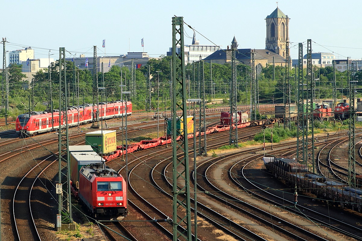 Während 185 397-7 am 04.07.2015 mit einem Containerzug in den Neusser Güterbahnhof einfährt, sind im Hintergrund zwei 440 als S 8 in Richtung Düsseldorf unterwegs