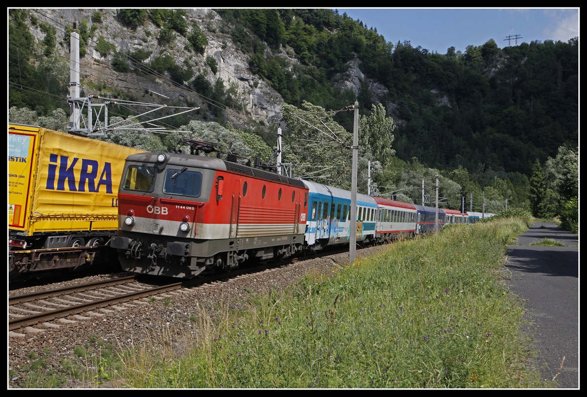 Während am Nachbargleis ein Zug der Rollenden Landstraße Richtung Bruck/Mur unterwegs ist, fährt 1144.063 mit EC151 Richtung Süden. Das Bild entstand am 23.06.2020 bei Peggau.