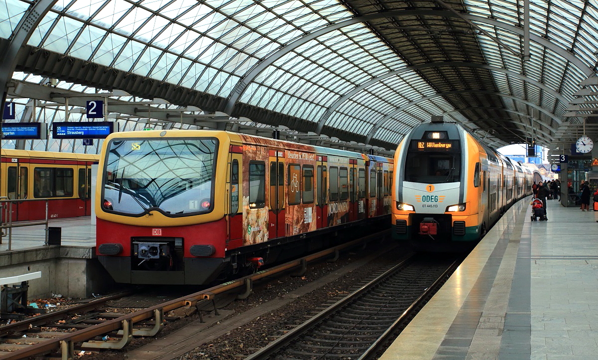 Während ein S-Bahn-Zug nach Strausberg am 21.11.2015 auf die Abfahrt wartet, verlässt der ODEG-ET 445.113 den Bahnhof Spandau in Richtung Wittenberge
