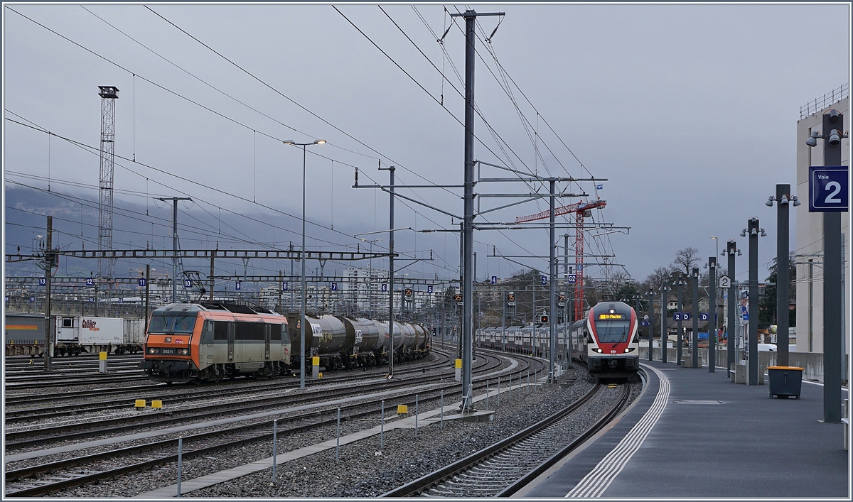 Während in Lancy Pont Rouge der RE 18441 von Annemasse nach St-Maurice, bestehend aus dem SBB RABe 511 110 und einem weiteren KISS eintrifft, wartet im Güterbahnhof Genève La Praille die SNCF Sybic BB 26 211 auf die Abfahrt. 

13. Februar 2020