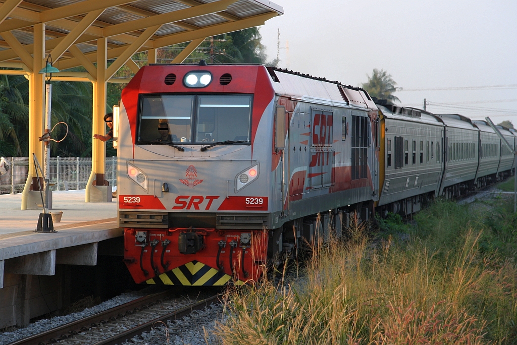 Während die QSY 5239 (Co'Co', de, CRRC Qishuyan, Bj.2023) am 09.Dezember 2023 mit dem SP.EXP 31  TAKSINARATH  (Krung Thep Aphiwat - Hat Yai Junction) durch die, infolge des 2 gleisigen Ausbau der Southern Line neu errichteten Ban Khu Bua Station fährt, schickt sich der Beimann an den Token vom Halter zu nehmen.