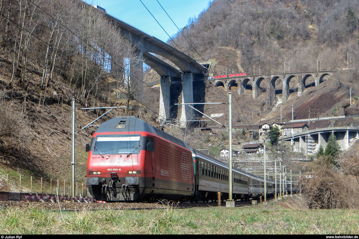 Während Re 460 093 am 16. März 2013 mit ihrem InterRegio gerade den Travi-Kehrtunnel in der Biaschina verlassen hat und nun den alten Bahnhof von Giornico auf der untersten Ebene passiert, fährt der nachfolgende Güterzug mit Re 6/6 11670 an der Spitze gerade auf den Pianotondo-Viadukt auf der obersten Ebene.
