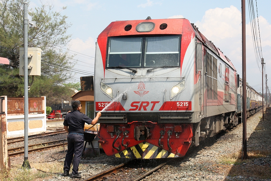 Während seine QSY 5215 (Co'Co', de, CRRC Qishuyan, Bj.2021) am 27.Februar 2026 vor dem RAP 102 (Chiang Mai - Krung Thep Aphiwat) in der Sila At Station betankt wird reinigt der Lokführer die Frontpartie seiner Lok.