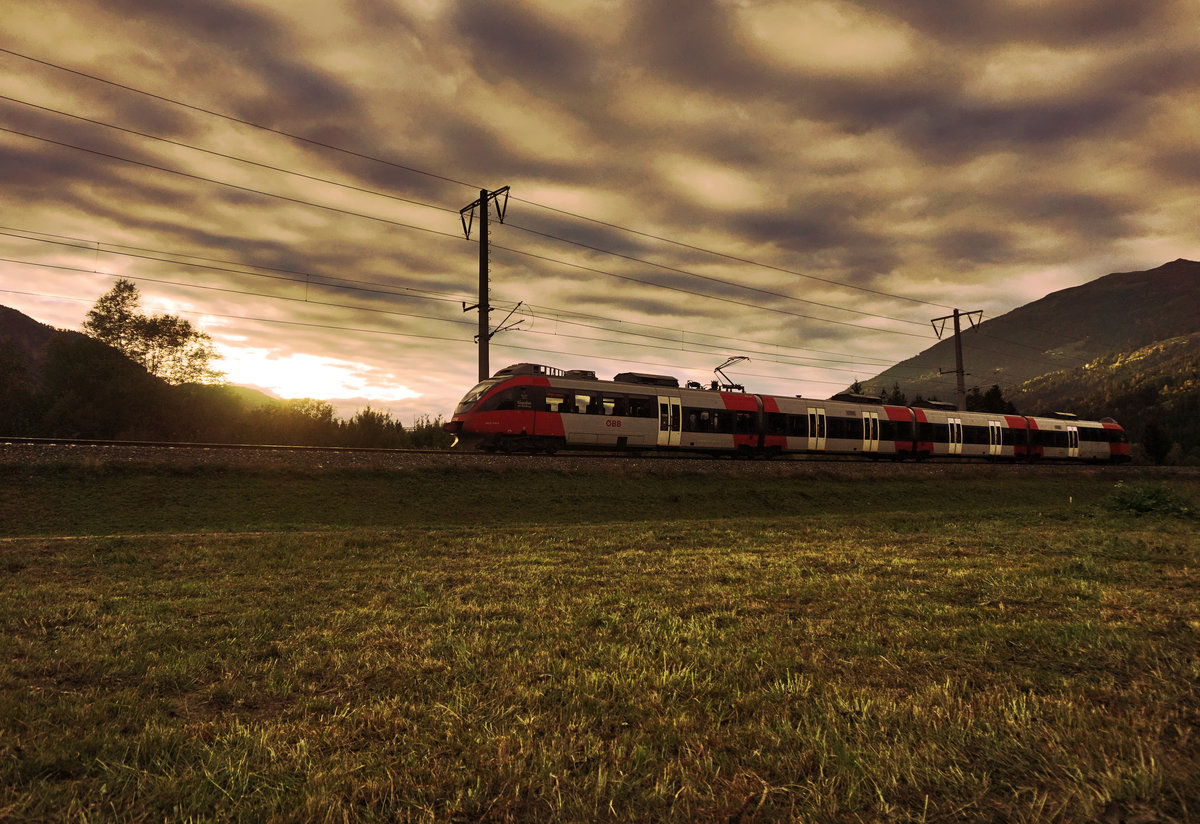 Während sich die Abendsonne vor dem Untergehen noch einmal durch die dichte Wolkendecke bahnte, ist 4024 114-3  Klagenfurt am Wörthersee  soeben als S1 4260 von Lienz nach Friesach unterwegs.
Aufgenommen am 6.10.2016, bei Berg im Drautal.