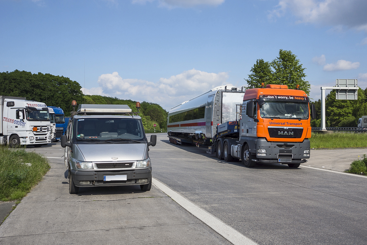 Wagenkasten eines neuen ICx-Mittelwagens auf einem Spezialtransporter auf dem Autobahnparkplatz Steinhausen an der A44 von Kassel nach Dortmund. Handschriftlich ist folgende Nummer angegeben: 3.X01-98-0850. Im Vordergrund links steht das Begleitfahrzeug zur Absicherung des Transports mit Übermaß. 16.05.2014