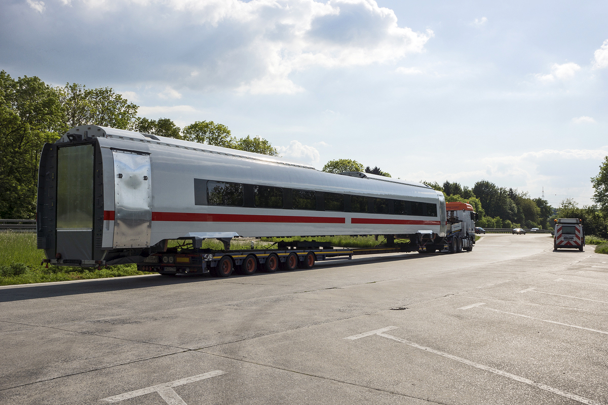 Wagenkasten eines neuen ICx-Mittelwagens auf einem Spezialtransporter auf dem Autobahnparkplatz Steinhausen an der A44 von Kassel nach Dortmund. Handschriftlich ist folgende Nummer angegeben: 3.X01-98-0850. Im Hintergrund rechts steht das Begleitfahrzeug zur Absicherung des Transports mit Übermaß. 16.05.2014