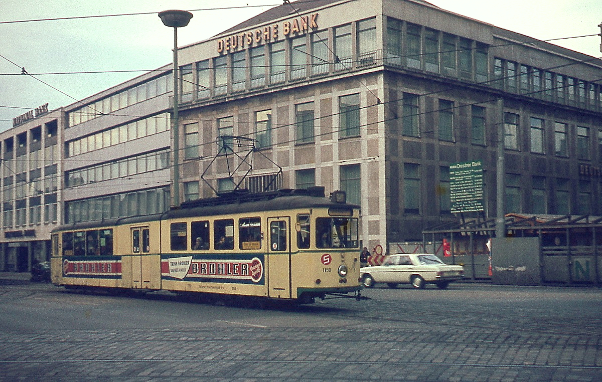 Wegen Personalmangel und fehlender finanzieller Mittel zur Beschaffung einer größeren Zahl von Neubau-Gelenktriebwagen baute die Duisburger Verkehrs-AG Ende der 1950er Jahre mehrere Zweiachser zu Gelenktriebwagen um. Am 20.12.1973 ist einer der 1925 gebauten Uerdinger Triebwagen mit einem gleichartigen Aufbau-Beiwagen und schwebenden Mittelteil als Tw 1159 an der Einmündung der Düsseldorfer Straße auf der Königstraße unterwegs. Heute ist die Königstraße zur Fußgängerzone umgebaut (Aufnahme mit einer Rollei 35-Kleinbildkamera).
