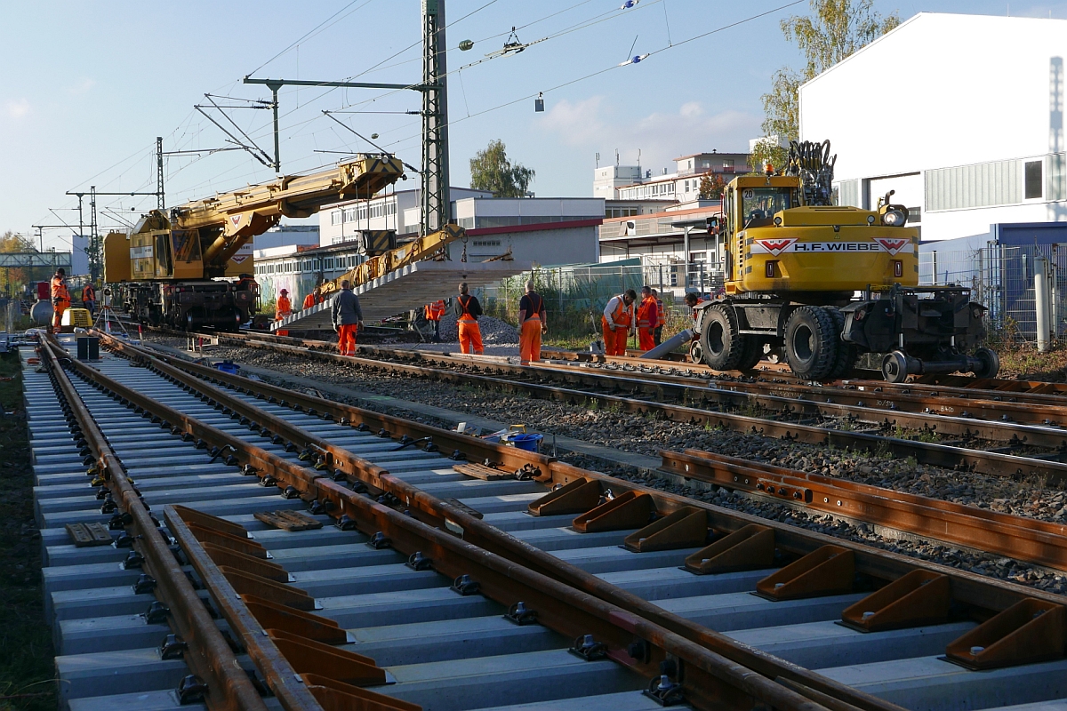 Weichenerneuerung in Konstanz-Petershausen - Gleisbauschienenkran (KRC 810 T, 99 80 9419 013-4 D-HFW) hat am 15.10.2016 das Verbindungsstck zwischen neuer Weiche und bestehendem Gleis am Haken und wird es in die zuschlieende Gleislcke einsetzen. Wird es passen?