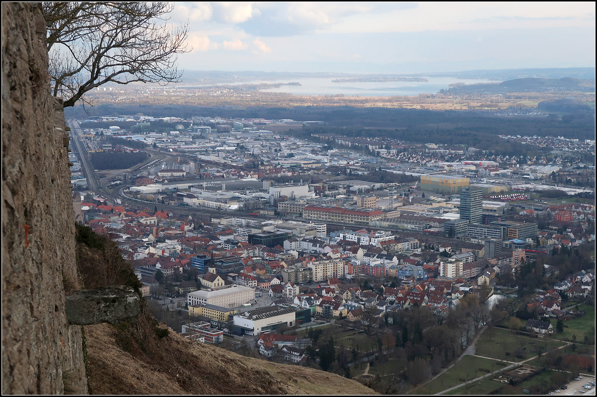 Wenn die Loknummern-Ablesung zur Herausforderung wird -

Blick von der Festung Hohentwiel auf Singen. Vor dem großen Gebäude in Bildmitte befindet sich der Bahnhof. Nach links oben kann man den Streckenverlauf in Richtung Radolfszell verfolgen. Rechts daneben der Güterbahnhof.

Im linken Bereich vom Bahnhof kann man eine rote Lok erkennen. Es handelt sich um die 185 244-1. Nahe dem rechten Bildrand sieht man zwei weitere Loks, die 185 138-5 und 185 125-2. Alle Nummern wurden von hier oben aus mit einem Spektiv abgelesen. Die Nummer der Lok ganz rechts von einem etwas anderen Standpunkt aus, hier ist sie von einem Baum verdeckt.

Im Hintergrund der Bodensee mit der Insel Reichenau. Auf dem Bild nicht, aber in Wirklichkeit kann man darüber neben dem Konstanzer Münsterturm auch den dortigen Bahnhofsturm erkennen.

04.02.2018 (M)

