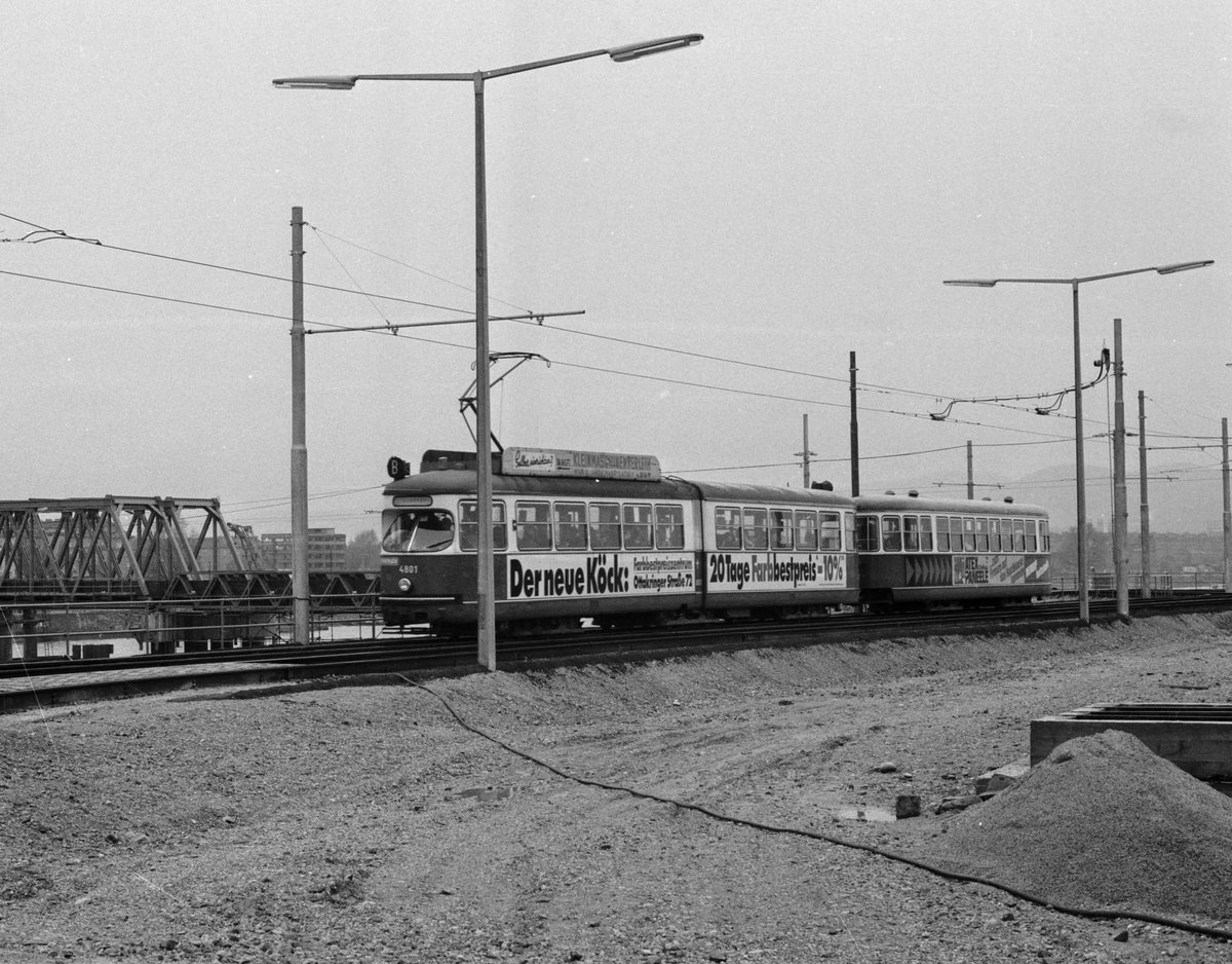 Wien am 31. Oktober 1976: Am Donaustädtischen Flussufer (22. Bezirk) befindet sich ein Zug der SL B (E1 4801 + c2/c3), der in Richtung Kaisermühlen fährt. - Im Hintergrund links ist ein Teil der Straßenbahnnotbrücke, des Ersatzes für die am 1. August 1976 in die Donau eingestürzte Reichsbrücke, zu sehen. - Der E1 4801 ist noch im Sommer 2016 in Betrieb. - Scan von einem S/W-Negativ. Film: Ilford FP 4. Kamera: Minolta SRT-101.