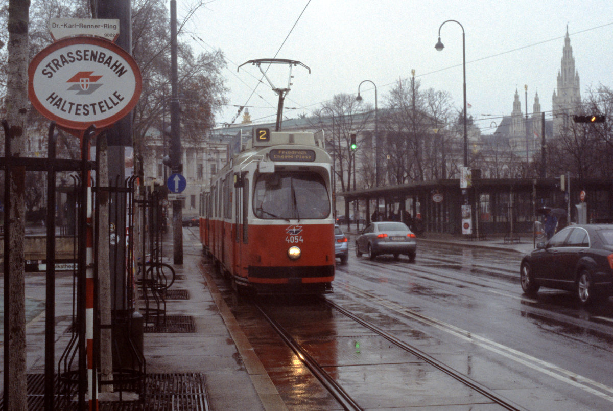 Wien Wiener Linien: An einem trüben Regentag im Februar 2016 erreicht der E2 4054 auf der SL 2 die Haltestelle Dr.-Karl-Renner-Ring im 1. Stadtbezirk. - Im Hintergrund lassen sich zwei wichtige Bauten sehen: das klassizistische Parlamentsgebaüde, das 1873 - 1883 vom dänisch-österreichischen Architekten Theophil Hansen erbaut wurde, und das Wiener Rathaus, das der Dombaumeister Friedrich Schmidt in den Jahren 1872 bis 1873 im neugotischen Stil errichtete. - Scan eines Diapositivs. Film: Fuji RXP. Kamera: Konica FS-1.