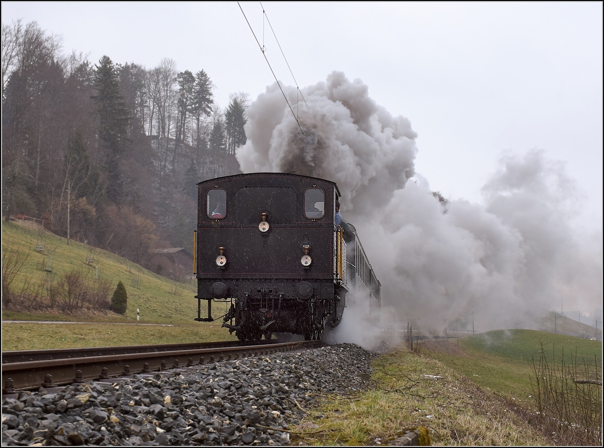 Winterdampf des Vereins Historische Emmentalbahn. Dampflok Ed 3/4 Nr. 2 der Solothurn-Münster-Bahn bei Dürrenroth. Mit im Gepäck hat sie zwei vierachsige Leichtstahlplattformwagen und einen K2. Vom Feldweg ist eine érstaunliche Position möglich, der ist hier mit einem Mäuerchen aus dem Bahndamm geschnitten. Februar 2018. 