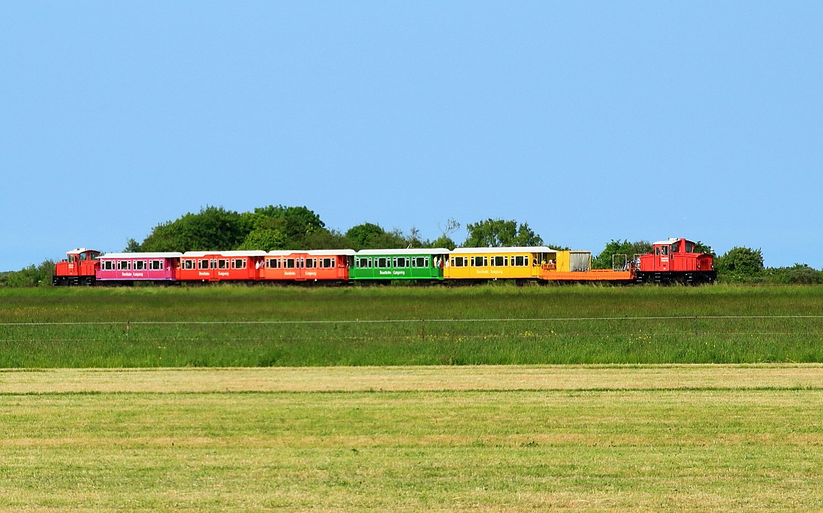 Ziemlich farbenfroh sind die Wagen der Inselbahn Langeoog lackiert, hier sind die Lokomotiven 4 und 2 zwischen Anleger und Inselbahnhof am 02.06.2017 unterwegs. Die von Schöma 1994/95 gebauten Lokomotiven ersetzten zusammen mit den 1994 von der Waggonfabrik Bremen beschafften Wagen die vorher hier eingesetzten Tiebwagen.