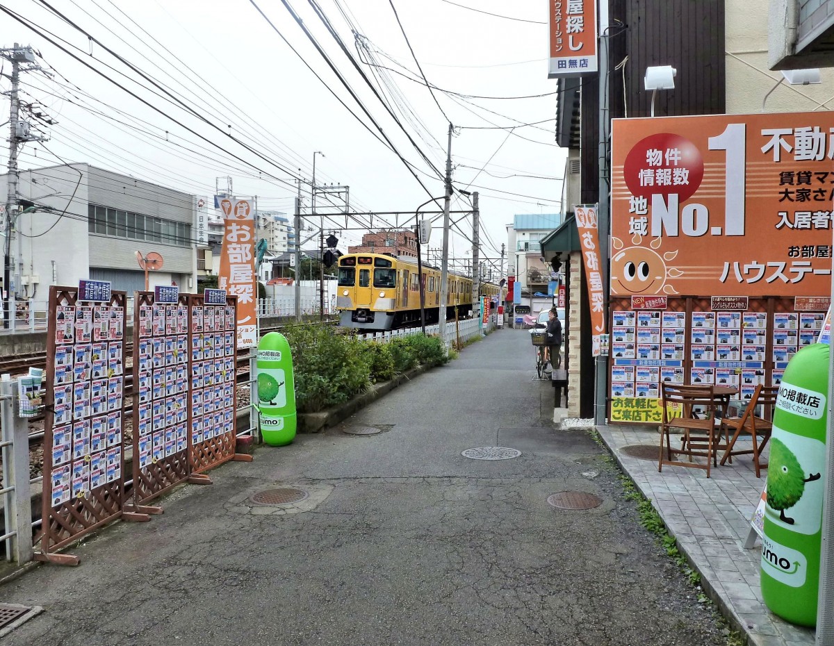 Züge des Seibu-Konzerns: Entlang der Seibu-Linie gibt es zahlreiche Häuser- und Wohnungsmakler; die jeweiligen Immobilien hängen als Bildchen mit allen Preisangaben aus. Im Hintergrund nähert sich der Seibu-Zug 2095 (Serie 2000). Tokyo-Tanashi, 11.Oktober 2011.  