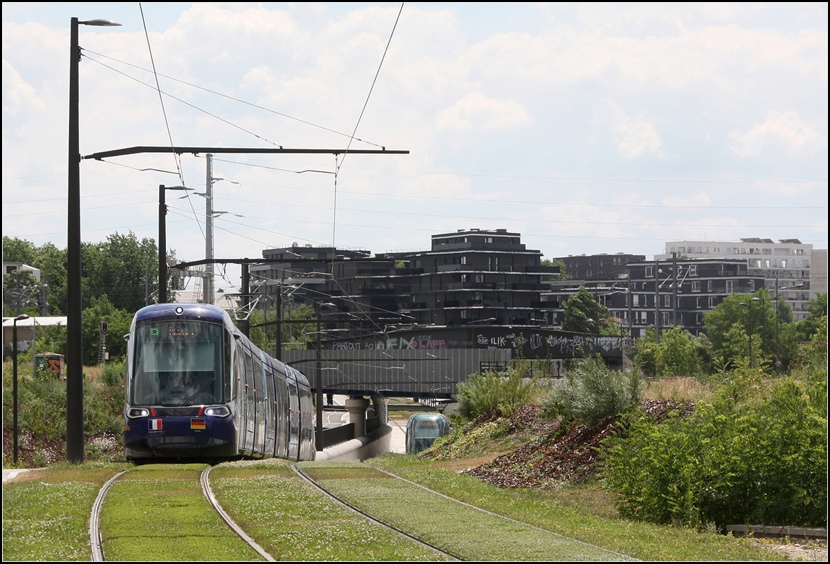Zuerst die Tram, dann die Stadt -

Die Verlängerung der Straßburger Tramlinie D nach Kehl führt im großen Bogen durch ein städtebauliches Entwicklungsgebiet im früheren Hafenbereich. Hier werden zwei Haltestellen noch ohne Halt durchfahren. Die Aufnahme entstand nahe der noch geschlossenen Haltestelle 'Starcoop' mit Blickrichtung Osten. Die Trasse senkt sich hier nach unten um die dortigen Bahnstrecken zu unterfahren.

25.06.2017 (M)