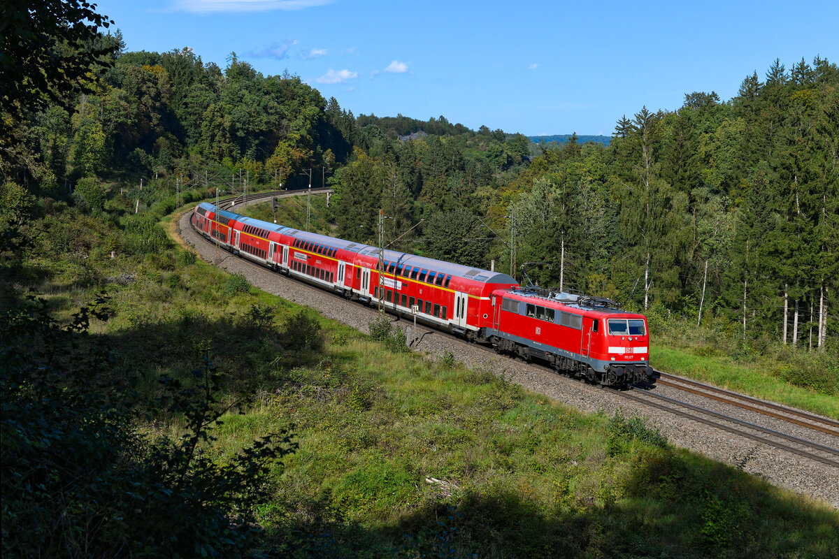 Zum Aufnahmezeitpunkt wurde der RE 59125 von Nürnberg HBF nach Augsburg HBF planmäßig aus einer Lok der Baureihe 111 und einer Garnitur Doppelstockwagen gebildet. Am 21. September 2023 war die 111 127 für diese Aufgabe eingeteilt. Im Waldstück bei Gundelsheim konnte ich den RegionalExpress mit ungewöhnlich hohem 1. Klasse-Anteil fotografieren. 
