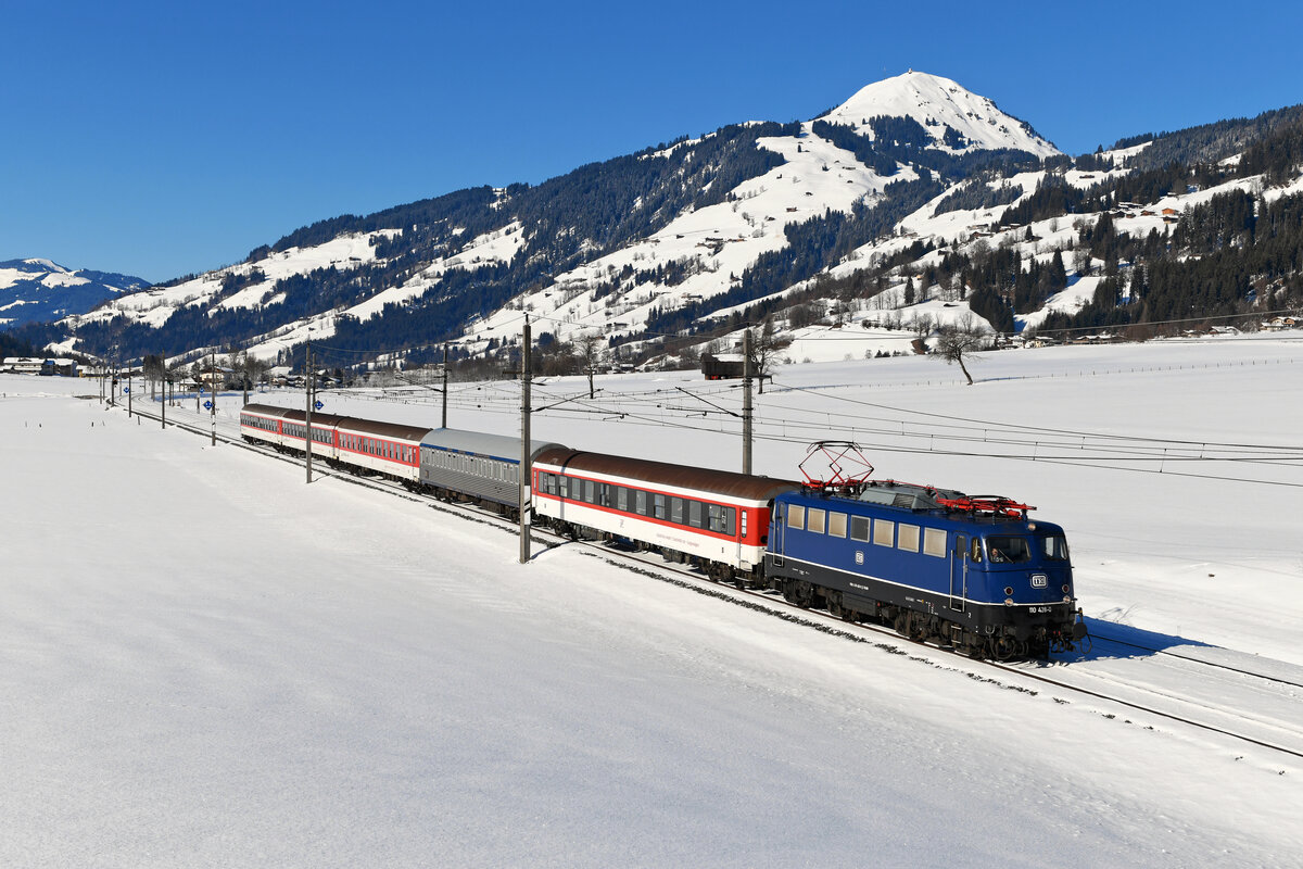 Zur Freude vieler Eisenbahnfreunde bespannte am 12. Februar 2022 die mustergültig gepflegte 110 428 von TRI den Alpen-Express ab Venlo. In Wörgl wurde der Zug dann geteilt. Die blaue Bügelfalte übernahm hierbei den Zugteil nach Bischofshofen. Wie so oft entwickelte sich das Warten auf den Zug als ziemliches Geduldspiel. Mit über zwei Stunden Verspätung erreichte der DRV 13489 gerade noch rechtzeitig meinen Fotostandpunkt bei Brixen im Thale - die Sonnenstand wäre sonst nicht mehr optimal gewesen. Die frisch verschneite Hohe Salve im Hintergrund bildete den angemessenen Hintergrund für diesen klassischen Turnuszug. Man fühlt sich in längst vergangene Zeiten zurück versetzt, als die es zum Standardgeschäft der Baureihe 110 gehörte, Schizüge auf der Giselabahn zu befördern. 