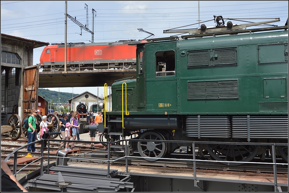 Zusammenkunft zweier Platzhirsche verschiedener Epochen. Ae 4/7 wird auf der Drehscheibe im Depot Brugg gedreht, während eine 185er der DB mit einem Gotthard-Güterzug über das Bahnhofsgelände von Brugg kreuzt. Mai 2015.