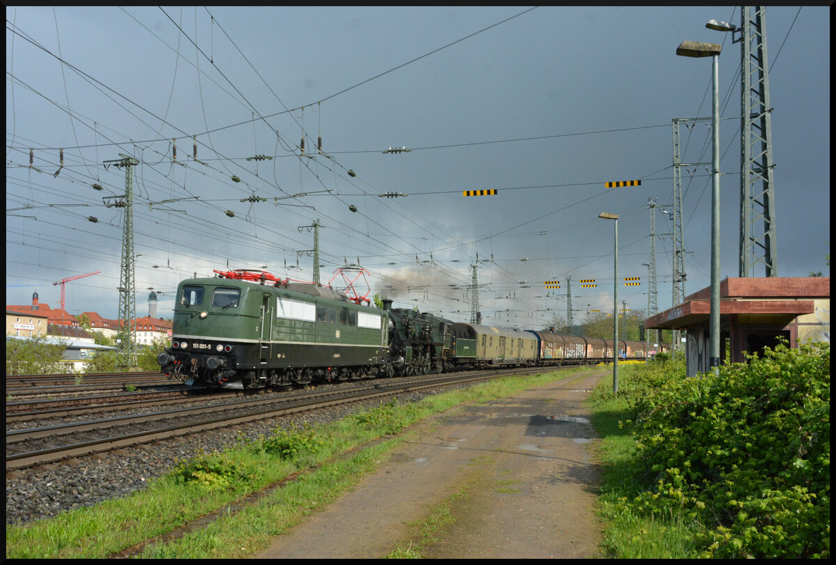 Zwei grüne Loks im Grünen – oder: Dualmode a la BayernBahn. Anlässlich der Museumstage am 20. & 21. April 2024 im DGEG Eisenbahnmuseum Bochum in Bochum-Dahlhausen überführte das Bayerische Eisenbahnmuseum Nördlingen (BEM) seine legendäre Schnellzugdampflok, die bayerische S3/6 3673, als Gastlokomotive von Bayern nach Nordrhein-Westfalen. Eingereiht in den ebenso bekannten Henkelzug fuhr die Dampflok am 18.04.2024 gemeinsam mit der BayernBahn 151 001 und einem ehemaligen Postwagen als Begleiter von Nördlingen über Donauwörth, Würzburg und Darmstadt-Kranichstein nach Bochum-Dahlhausen.
Die beiden grünen Lokomotiven konnten bei der Überführungsfahrt, sozusagen als Dualmode-Gespann a la BayernBahn, in Würzburg im Grünen beobachtet werden.

