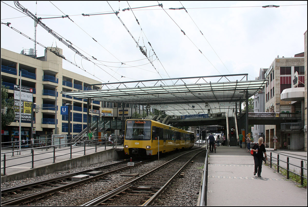 Zweistufiger Wandel - 

Seit der Aufnahme von Kurt im Jahre 1979 veränderte die Haltestelle Wilhelmsplatz in Stuttgart-Bad Cannstatt zweimal ihr Aussehen: 

http://www.bahnbilder.de/bild/deutschland~strassenbahn~stuttgart-keine-stadtbahn/654099/stuttgart-ssb-sl-2-dot4-925.html 

Anfang der 80iger Jahre entstand die Fußgängerbrücke, die die Bahnsteige der Straßenbahn mit der S-Bahnstation am Bahnhof Bad Cannstatt verbindet. Gleichzeitig wurde die Haltestelle modernisiert und für den Stadtbahnbetrieb vorbereitet: Schotterbahnkörper, neue Unterstände. 1986 wurde dann die Linie 1 auf Stadtbahnbetrieb umgestellt. Wegen des Mischbetriebes mit der Straßenbahn wurden aber keine Hochbahnsteige gebaut. Damals war es noch das Konzept, Hochbahnsteige nur dort zu errichten, wo es kein Mischbetrieb gibt und wo es städtebaulich relativ unproblematisch war, zum Beispiel entlang eigener Bahnkörper. 

Die Hochbahnsteige entstanden dann im Zusammenhang mit der Umstellung der Linie 2 auf Stadtbahnbetrieb im Jahr 2002. Gleichzeitig wurde die Haltestelle samt Fußgängerbrücke großzügig überdacht. 

23.06.2016 (M)