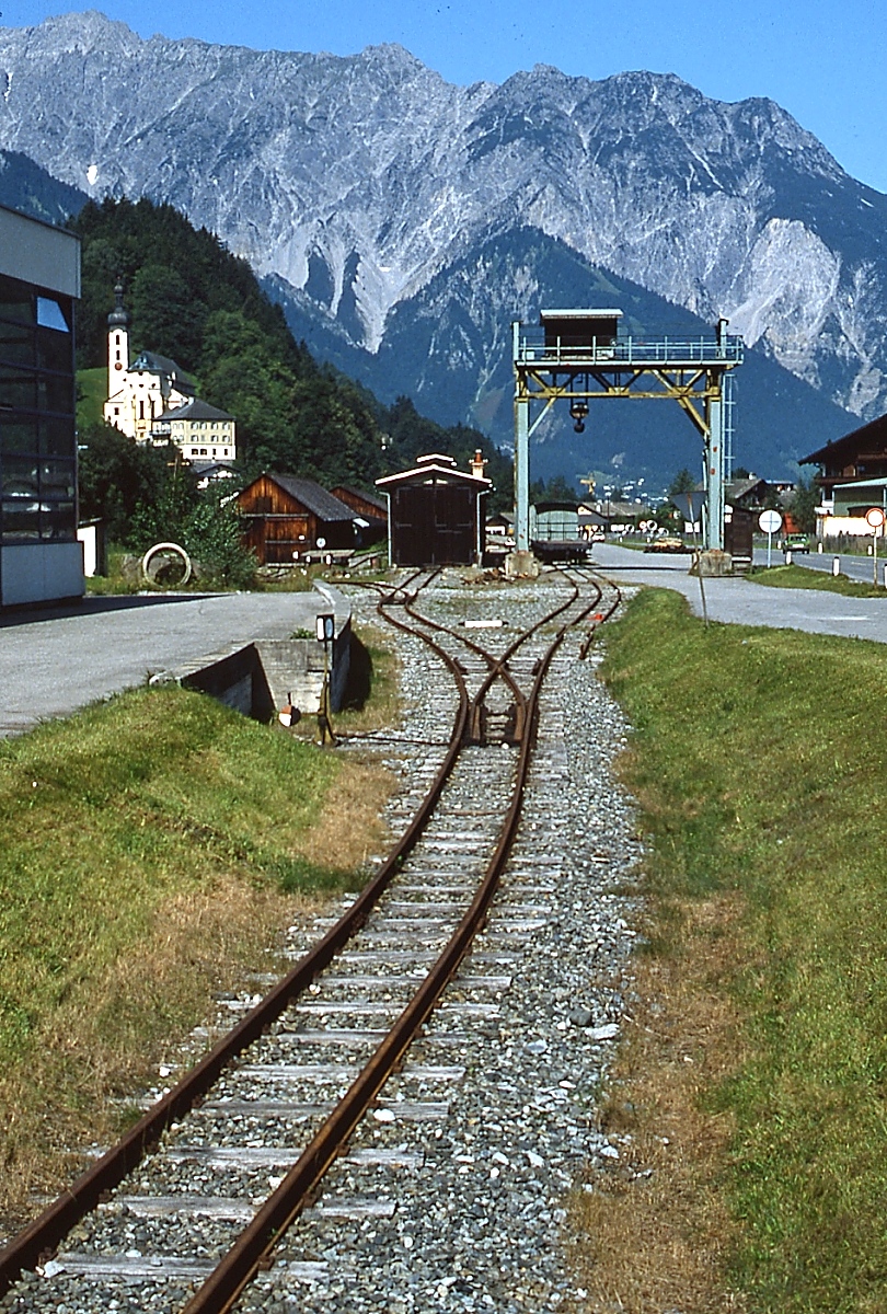 Zwischen 1927 und 1961 betrieben die Vorarlberger Illwerke eine 760 mm-Schmalspurbahn, die vom Bahnhof Tschagguns an der Montafonerbahn nach Partenen führte. Sie diente dem Materialtransport zu den beiden Kraftwerken in Vermunt und Obervermunt und dem Silvrettastausee. Der planmäßige Betrieb, auch Personenverkehr, endete 1953. Nach der Einstellung wurden die Gleise bis auf ein etwa 500 m langes Reststück, das bis 2001 zur gelegentlichen Materialanlieferung für die Illwerke diente, abgebaut. Teilweise wurde der Oberbau für den Ausbau der Stainzerbahn verwendet. Bis 2011 wurde in dem in der Bildmitte sichtbaren Lokschuppen das Motorboot  Silvretta , das im Sommer auf dem Silvretta-Stausee verkehrte, im Winter abgestellt. 2013 wurden die noch vorhandenen Anlagen abgebaut. Die Aufnahme entstand im August 1982 in Tschagguns.