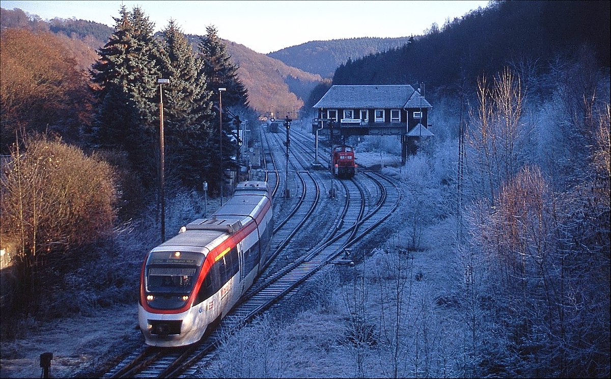 Zwischen 1999 und 2004 betrieb die Dortmund-Märkische Eisenbahn die Strecke von Dortmund über Hagen nach Lüdenscheid. Kurz vor Auslaufen des Vertrages mit dem VRR verlässt einer der vier dreiteiligen Talent-Triebwagen der DME Anfang Dezember 2004 Brügge (Westfalen) in Richtung Dortmund Hauptbahnhof. Vor dem Reiterstellwerk ist 294 295-1 abgestellt. An den kürzesten Tagen des Jahres erreicht die tiefstehende Sonne nicht den Bahnhof und so hielt sich der Raureif dort bis zum Nachmittag.
