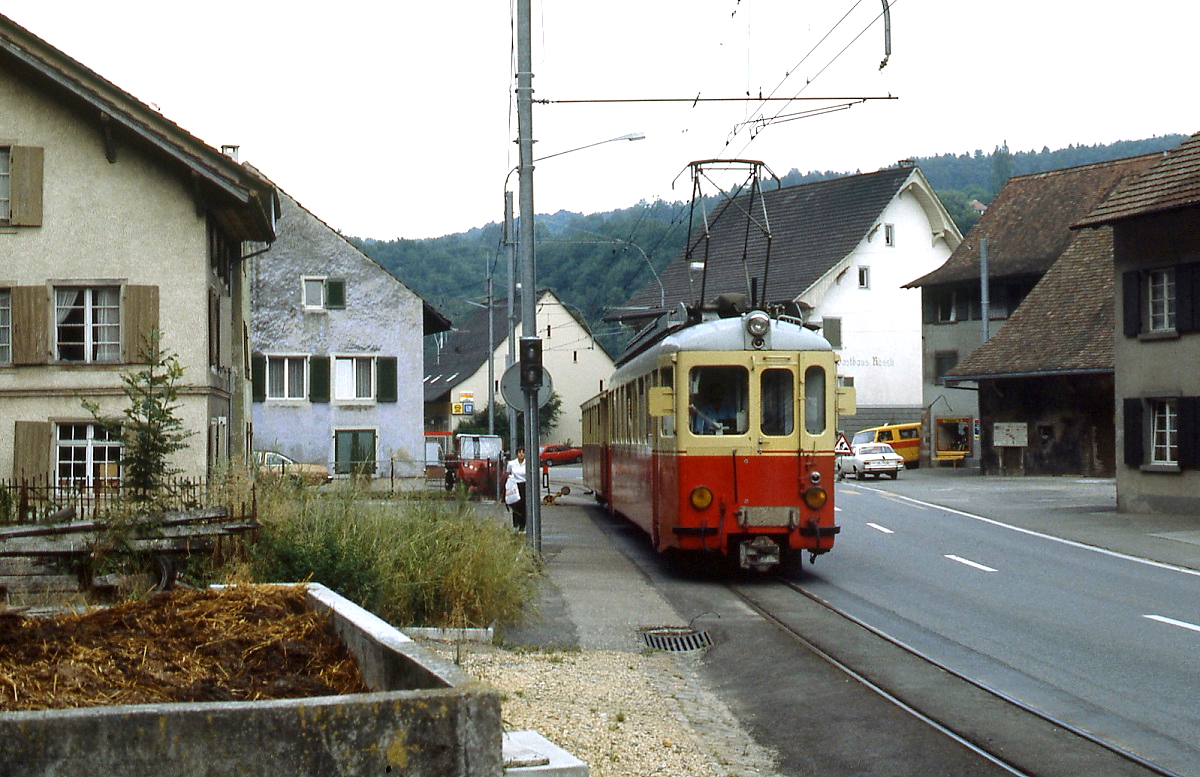 Zwischen Misthaufen und Straße ist BDe 4/4 1 oder 2 der Waldenburgerbahn im Juli 1983 in Hölstein unterwegs. Die BDe 4/4 1-3 wurden 1953 beschafft, nachdem die Waldenburgerbahn elektrifiziert wurde, 1986 wurden sie durch Neubaufahrzege ersetzt. Als einzige schweizer Bahn hat die Bahn die Spurweite von 750 mm.