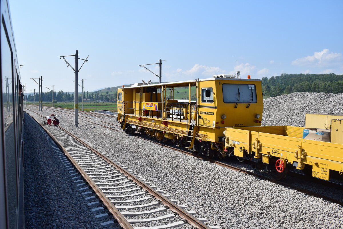 Zwischen Ormenis und Apata fädelt der neutrassierte Abschnitt von Racos nach Apata in die Bestandsstrecke ein und führt bis Apata 4gleisig. Im neuen Streckengleis Apata nach Racos steht ein dynamischer Gleisstabilisator des Types DGS 62 N. Dieser simuliert durch Vibrationen die notwendigen Lasttonnen nach einem Stopfgang. Somit wird keine Langsamfahrstelle notwendig bis die Lasttonnen erreicht sind. Weiter vorne im Nachbargleis sieht man 2 Schweißer welche soeben eine Schweißung schleifen.

Apata 02.09.2025