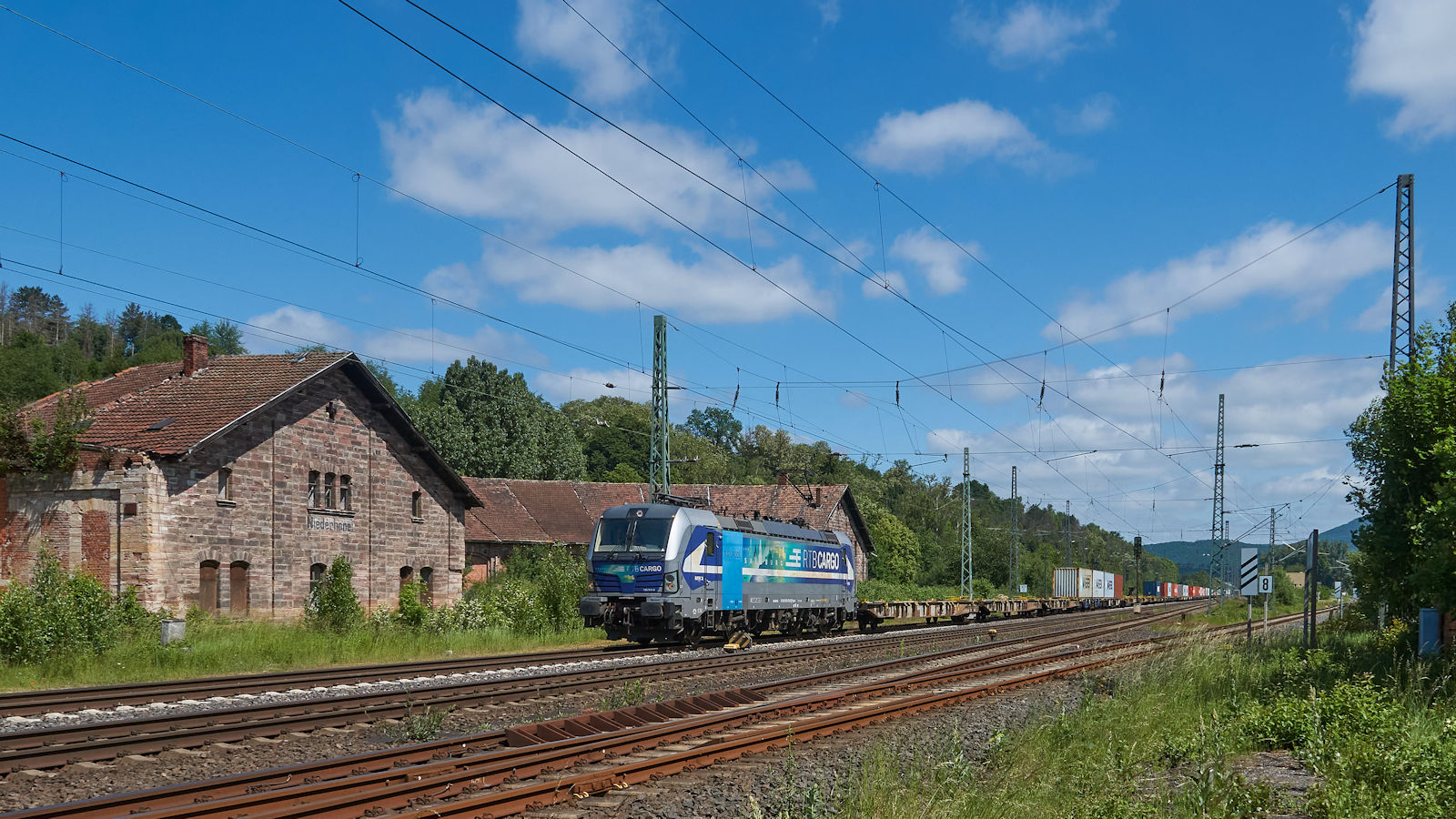 193 564 von RTB Cargo zog am 13.06.2021 einen Containerzug über die alte Nord-Süd-Strecke durch den ehemaligen Bahnhof Eschwege-West mit seinem historischen Ringlokschuppen. Dieser wurde 1875 erbaut und bis 1965 als Lokschuppen genutzt. Derzeit wird die Anlage restauriert.