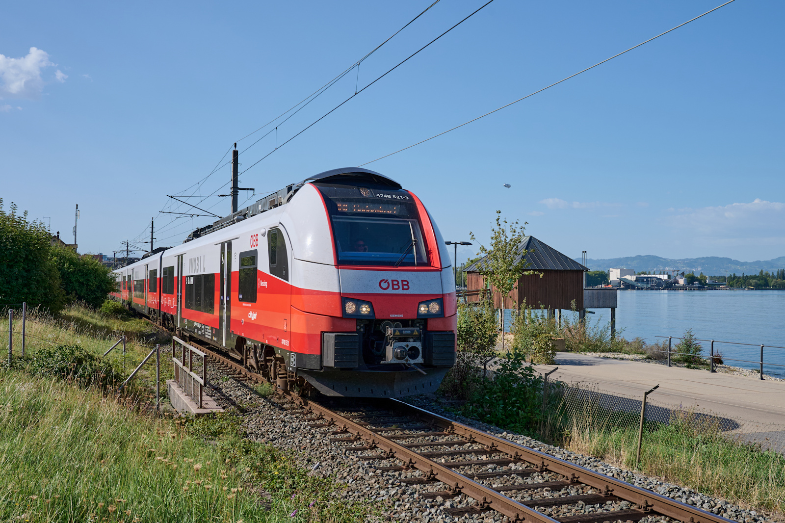 4748 521 war am 08.09.2026 als S25916 auf dem Weg von Bludenz nach Lindau. Gerade hat der Zug den Bahnhof Bregenz Hafen hinter sich gelassen und f�hrt am Bodensee entlang in Richtung Deutschland. 
