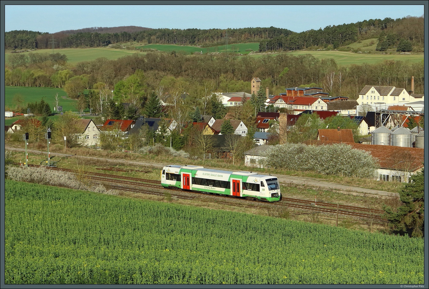 650 412-9 (VT 012) der Erfurter Bahn erreicht am 06.04.2024 den Bahnhof Stadtilm. Hinter dem Zug sind die Häuser des Stadtteils Oberilm und das Waschmittelwerk zu sehen.