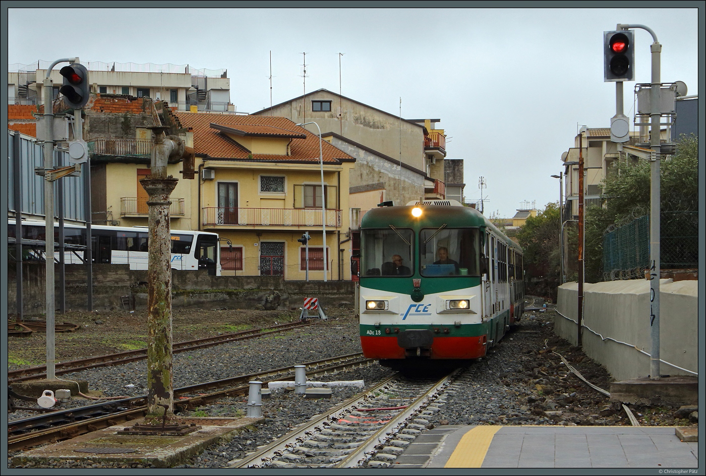 ADe 18 der FCE fährt am 28.02.2024 in Paternò ein. Links ist ein Bus der FCE zu sehen, diese verkehren vielfach parallel zur Bahn.