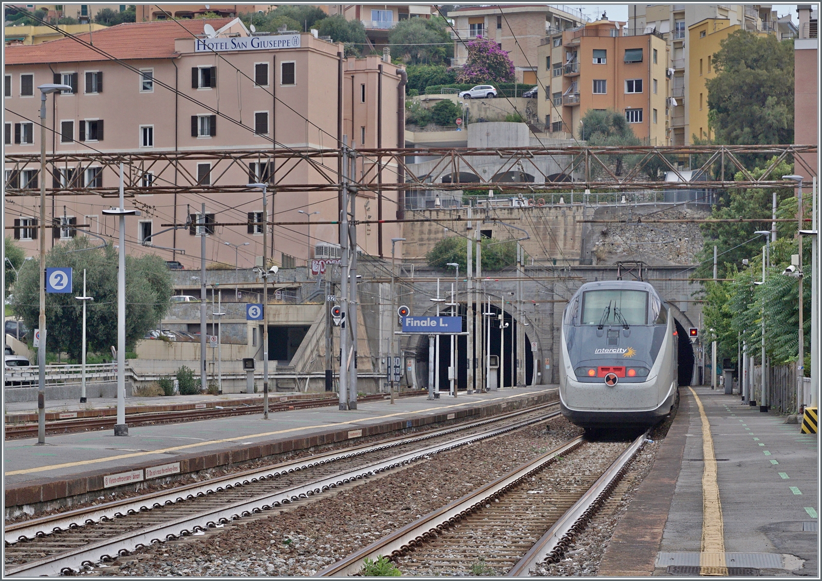 Als vor wenigen Jahren bei Cervia eine der schönsten Streckenabschnitte der Strecke Genova - Ventimiglia durch eine Tunnel-Variante ersetzt wurden, reiste im Vorfeld nochmals zahlreiche Fotografen an. Die 1868 eröffnete Strecken Genova - Savona. bzw. 1972 in Betrieb genommene Fortsetzung Savona Ventimiglia führte vielerorts durch eine schwierige Topografie und wurde grösstenteils dem Meer entlang und durch die Ortschaften trassiert. In den 1960er genügte die Einspur-Strecke dem Meer entlang nicht mehr dem zunehmenden Verkehr, so das im Raum Genova erste Neubautrassierungen erfolgen. 1977 folgte mit dem Abschnitt Varazzo - Finale Ligure ein erste länger Neubauabschnitt. Mit der Zeit folgten weiter westlich weitere, doch in Finale Ligure treffen sich nun der erste Neubauabschnitt mit dem letzten noch ursprünglichen Streckenabschnitt. Dies ist auch das Motiv der Bilder von Finalie Ligure, hier verlässt der FS Trenitalia IC 631 Finale Ligure und fährt in die nun seit 1977 neu trassierte Strecke ein, welche an den beiden Doppelspurportalenden der  Gallerie San Bernardino  zu erkennen ist. Die  Gallerie San Bernardino  ist 730 Meter lang, nach einem kurzen offenen Abschnitt folgt dann die 6514 Meter lange  Galleria San Giacomo.  

16. September 2023