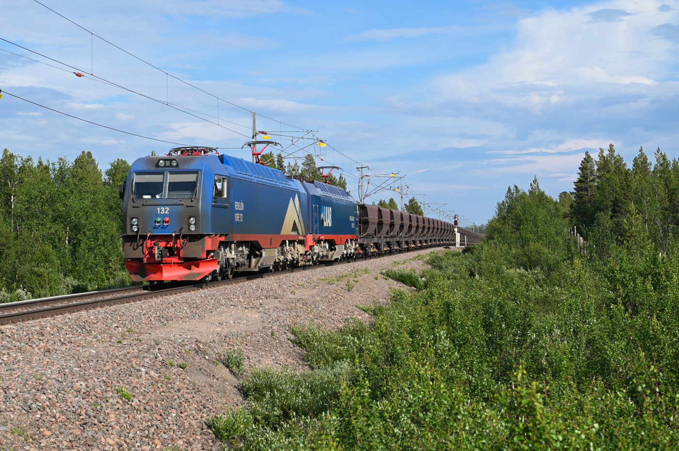 Am 02.07.2022 ist dieser voller Erzzug mit rund 8600 t Gewicht in Richtung Narik unterwegs und erreicht soeben den Bahnübergang bei Rautas. Das mit den ca. 20 Zügen am Tag transportierte Erz macht rund 50% des gesamten schwedischen Güterverkehrs aus (bezogen auf das Gewicht).
