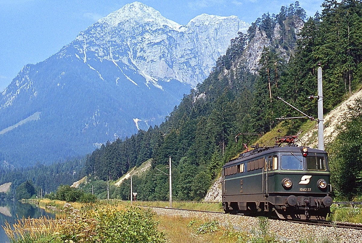 Am 25.08.1980 fährt 1042.37 als Lz durch das Gesäuse am damaligen Haltepunkt Kummerbrücke entlang der aufgestauten Enns in Richtung Hieflau, im Hintergrund der Große Buchstein (2.224 m). Anmerkung: Ein leicht ins Fahrwerk reichender Strauch wurde digital beschnitten.