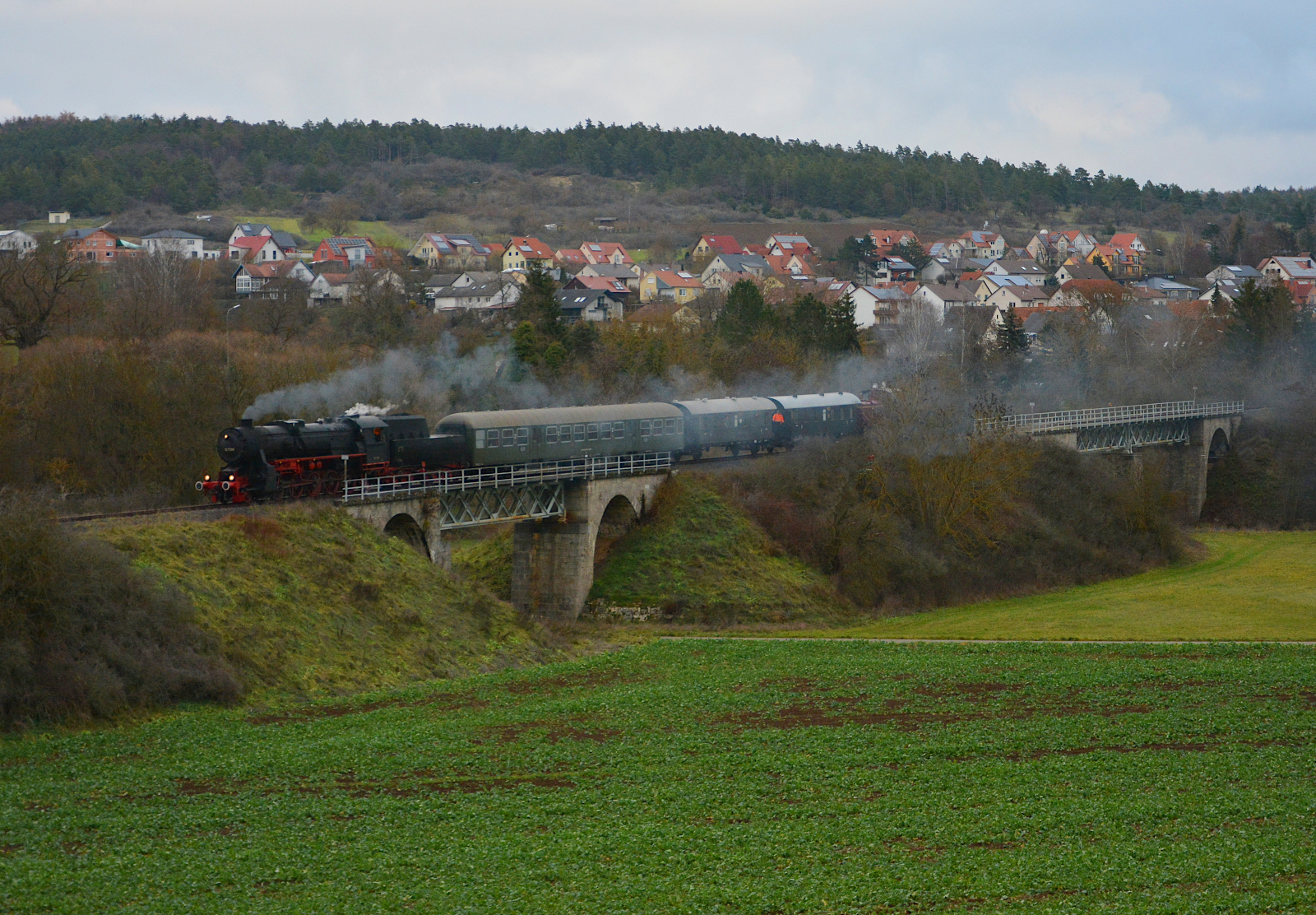 Am dritten Adventswochenende (10. - 11.12.2022) weilten die Eisenbahnfreunde Zollernbahn (EFZ) mit ihren Dampflokomotiven 01 519 und 52 7596 bei den Spur1-Tagen in Mellrichstadt. Die Güterzugmaschine 52 7596 bespannte gemeinsam mit der V60 734 des Fränkischen Freilandmuseums – FFM das „Rhön-Zügle“, bestehend aus zwei 3. Klasse Donnerbüchsen des FFM und dem Bn-Wagen der NeSA, zwischen Mellrichstadt und Ostheim bzw. Fladungen. Hier überquert der Zug auf einer Fachwerkbrücke bei Stockheim (Rhön) das Flüsschen Streu. HINWEIS: Eine quer durch die Szenerie laufende Freileitung wurde digital entfernt.