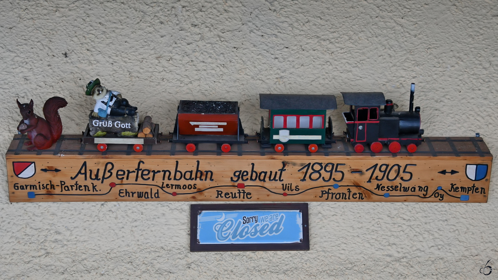 Am ehemaligen Bahnhof Pfronten-Steinach wird mit dieser Holzarbeit an die Bauzeit der Außenfernbahn erinnert. (November 2023)