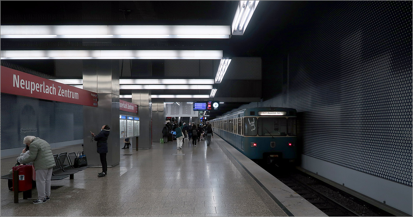 Aufgefrischt - 

... werden bei der Münchner U-Bahn derzeit auch Stationen der 1980 eröffneten Strecke vom Scheidplatz über Hauptbahnhof, Sendlinger Tor und Innsbrucker Ring nach Neuperlach-Süd. Diese Strecke mit insgesamt 18 Bahnhöfen ist die längste U-Bahnstrecke, die je in Deutschland auf einen Schlag eröffnet wurde. Nur der Endbahnhof Neuperlach-Süd liegt oberirdisch.

Im Bild die schon modernisierte Station 'Neuperlach-Zentrum,' mit neuen Verkleidungen der Hintergleiswänden. Ursprünglich hatte man vom mittig angeordneten Zwischengeschoss Blickverbindung zum hier recht breiten Bahnsteig. Diese galerieartige Öffnung wurde aus brandschutztechnischen Gründen inzwischen leider zugemauert.

09.11.2022 (M)