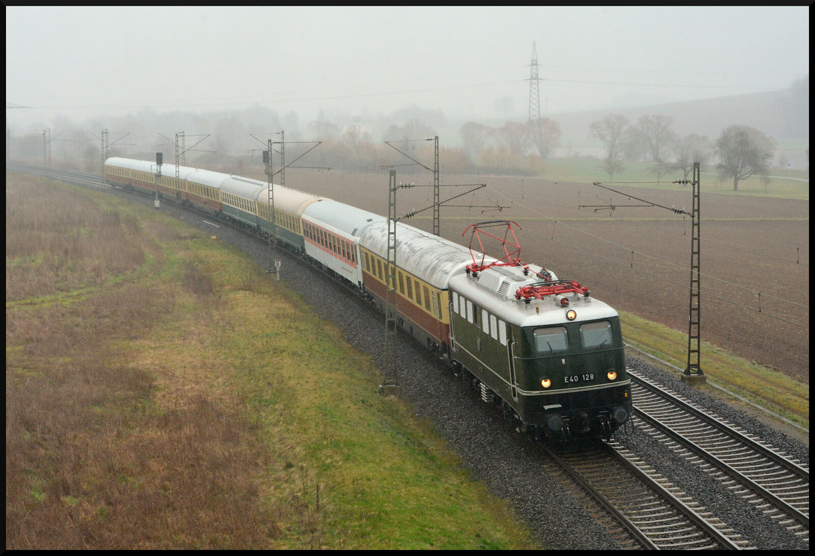 Bei trübem Regenwetter ist die E40 128 mit einem bunten Wagenpark am 12.03.2023 als Lr 5604 von Crailsheim über Ansbach, Würzburg, Gemünden, Darmstadt Kranichstein nach Koblenz-Lützel ins dortige DB-Museum unterwegs gewesen, als der Zug im Maintal bei Harrbach fotografiert werden konnte. 