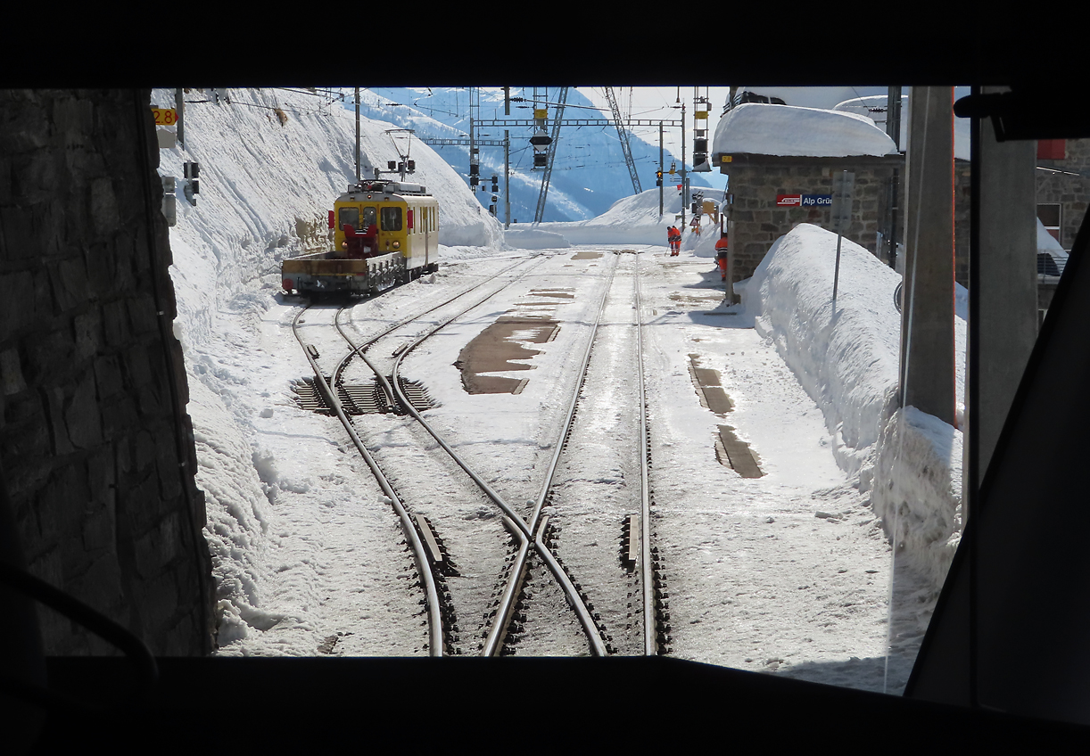 Blick aus dem 1. Klass-Abteil hinter dem Führerstand im Regionalzug von St. Moritz nach Tirano bei der Einfahrt in den Bahnhof Alp Grüm (2091 müM). Links wartet ein Oldie-Triebwagen in der alten Farbgebung der Berninabahn mit einem Arbeitszug auf seinen Einsatz. Alp Grüm, 19.2.2021