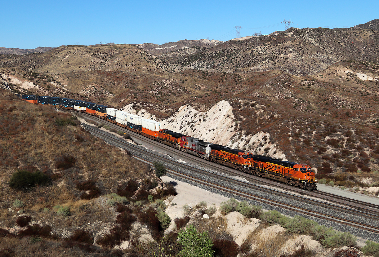Containerzug fährt auf der südlichen Seite des Cajon Passes in die Sullivan's Curve. Diese Zug fährt auf der mittleren Linie der BNSF talwärts, im Vordergrund sieht man die UP-Linie, an dieser Stelle doppelspurig. Cajon Pass, CA, 22.9.2022